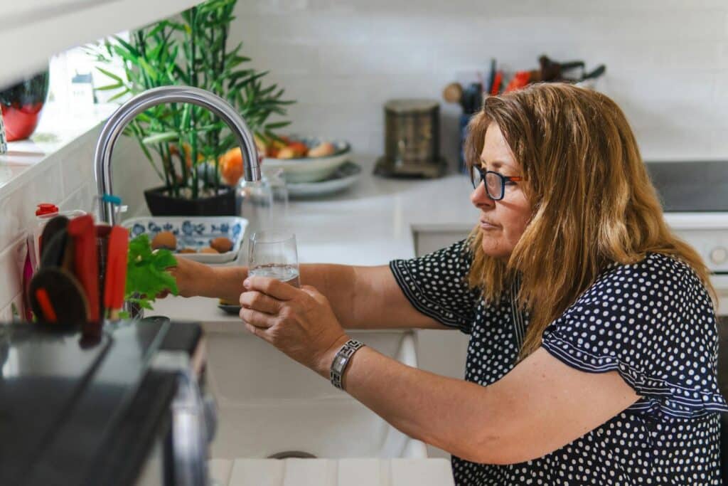 A middle-aged woman filling a glass with water in a modern kitchen setting.