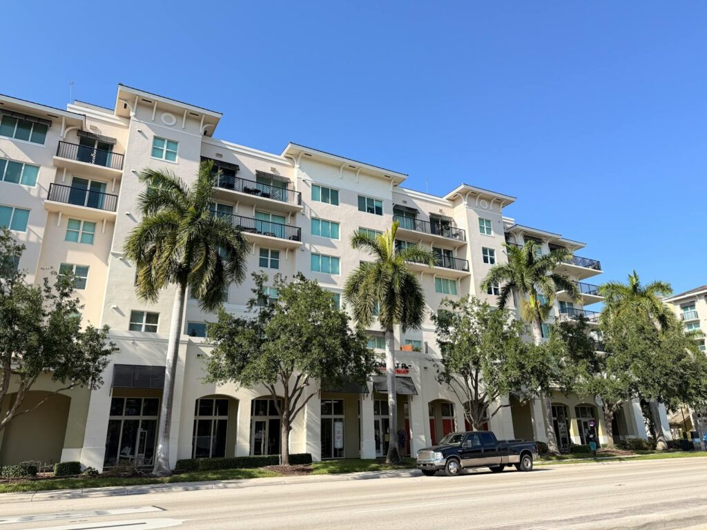 A modern apartment building with palm trees on a clear sunny day.